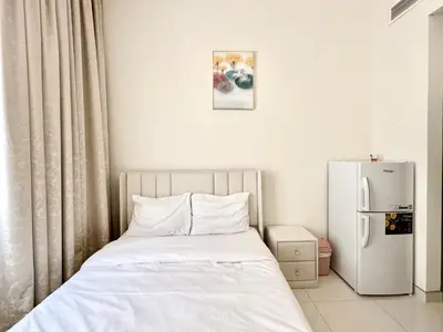 a bedroom with a white bed and a refrigerator at Al Manara Premium Cozy Studio in Dubai