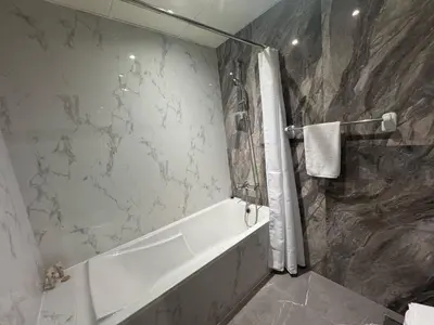 a bathroom with a white tub and a marble wall at Chic Studio with Balcony a mins drive to Downtown in Dubai