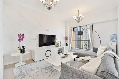 a white living room with a couch and a tv at Bright and Spacious 2BR with Pool and Gym Access in Dubai