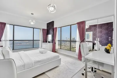a bedroom with a white bed and a desk and windows at Bright and Spacious 2BR with Pool and Gym Access in Dubai