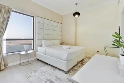 a bedroom with a white bed and a large window at Bright and Spacious 2BR with Pool and Gym Access in Dubai