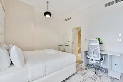 a white bedroom with a white bed and a desk at Bright and Spacious 2BR with Pool and Gym Access in Dubai