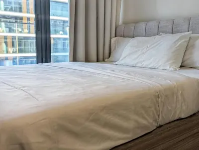 a large bed with white sheets and a window at Fully Furnished Modern Studio Apartment Nearby Meydan Racecourse in Dubai