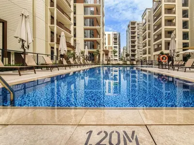 a swimming pool with chairs and umbrellas next to buildings at Modern one bedroom apartment in lotus creek beach in Dubai