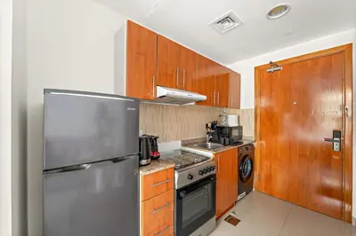 a kitchen with a stainless steel refrigerator and wooden cabinets at FIRST CLASS Studio Cozy & Chic Retreat in Dubai