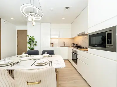 a white kitchen with a dining table and chairs at Palace residence creek harbour in Dubai