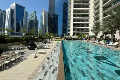 a large swimming pool with chairs and tables and buildings at Modern and Relaxing 1 Bedroom in Zada Tower in Dubai