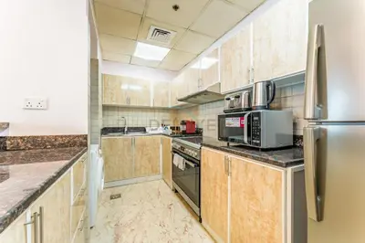 a kitchen with wooden cabinets and a stainless steel refrigerator at Affordable Living 1BR, Steps from Retail Stores, Skycourts Tower D, Dubailand by Deluxe Holiday Homes in Dubai