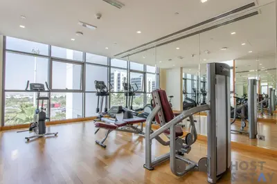 a gym with treadmills and ellipticals in a room with windows at Elegant Studio Without Balcony- Damac Hills, Dubai - Host & Stay in Dubai