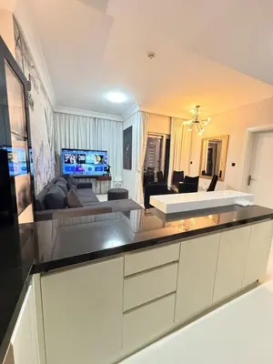 a kitchen with white cabinets and a living room at 1 BR in Mall St in Dubai