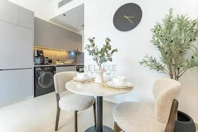 a dining room with a table and chairs and a clock at Community Views Studio Near Nad Al Sheba Gardens with Balcony, MAG 980, Mohammad Bin Rashid by Deluxe Holiday Homes in Dubai