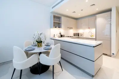 a kitchen with white cabinets and a table and chairs at Premium Chic Fully Furnished 1 BR in Sobha Hartland in Dubai
