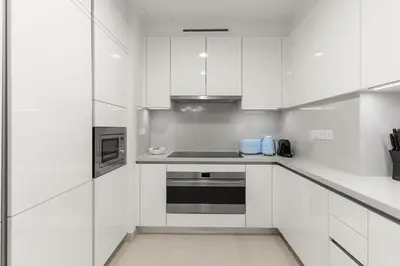 a white kitchen with white cabinets and appliances at Elegant 1BR Apt with Balcony Views of Burj Khalifa & Dubai Canal in Dubai