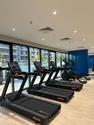 a row of treadmills in a gym with windows at Azizi riviera luxury studio apartment monthly rent in Dubai