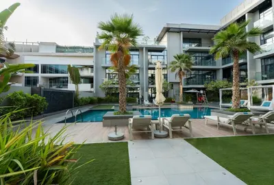 a large building with a swimming pool and palm trees at Stylish Retreat - Embrace the Comfort in Dubai