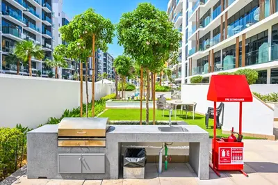 a barbecue grill with a red object next to a building at Cozy Studio with Balcony in Azizi Riviera and 10 Mins to Burj Khalifa in Dubai