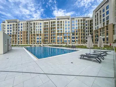 a large apartment building with a swimming pool and two umbrellas at Stunning 1BR APT in Rukan with Gym and Pool in Dubai