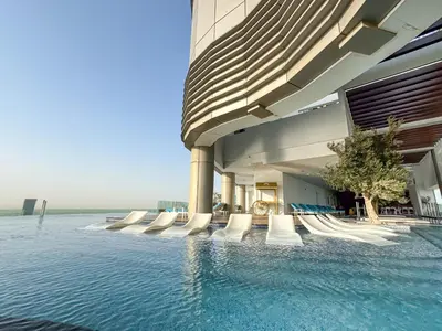 a building with a swimming pool next to the water at Stunning Burj View - High Infinity Pool - Cozy 2BR in Dubai