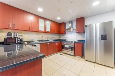 a kitchen with wooden cabinets and a stainless steel refrigerator at Close to Major Landmarks 3BR and Assistant Room with Marina Views, Rimal 5, JBR by Deluxe Holiday Homes in Dubai
