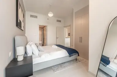 a white bedroom with a bed and a mirror at HAVN - 1 Bed in Damac Hills 1, Golf Course View in Dubai