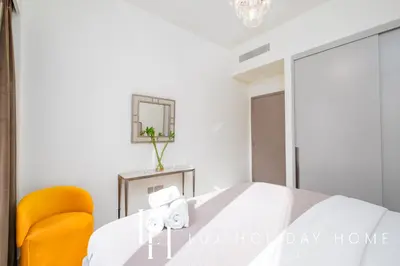 a white bedroom with a bed and a yellow chair at LUX The Grande Signature Skyline Suite 2 in Dubai