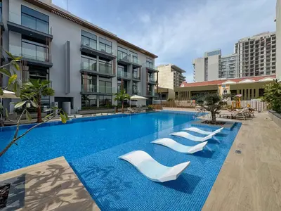 a swimming pool with white chairs and a building at Luxury Loft with Balcony in JVC, Oxford Terraces 2 in Dubai