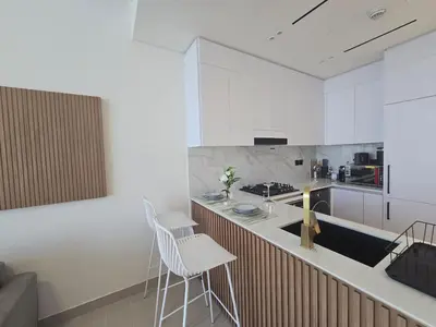 a kitchen with white cabinets and a counter with chairs at Luxury & Comfort at Binghatti Amber with Balcony in Dubai