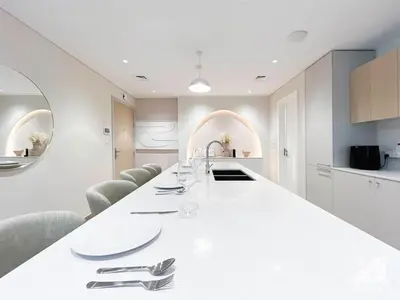 a white kitchen with a long white table and chairs at Sophisticated 1B Apartment in Belgravia Heights II in Dubai