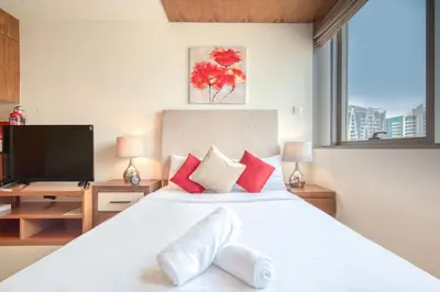 a bedroom with a white bed with red pillows and a tv at Restful studio Apartment in Dubai Sports City in Dubai