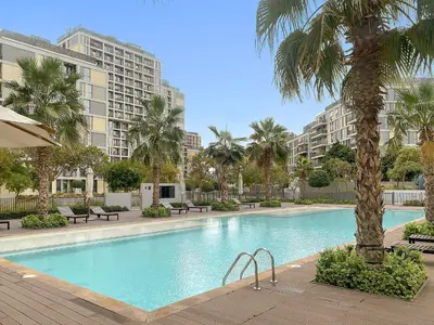 a large swimming pool with palm trees and buildings at Silkhaus Signature 1BR in Afnan at Production City in Dubai