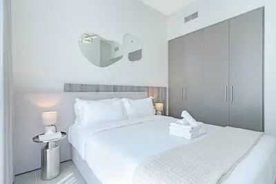 a white bedroom with a large white bed and a lamp at Sky-High Downtown 1BR Steps from Burj Khalifa in Dubai