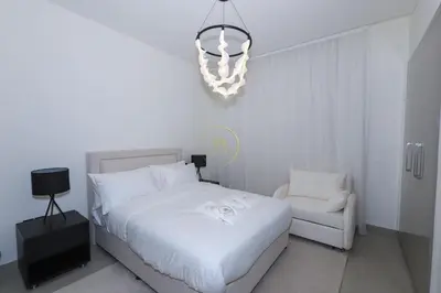 a white bedroom with a white bed and a chandelier at Sobha Hartland Waves-912 in Dubai