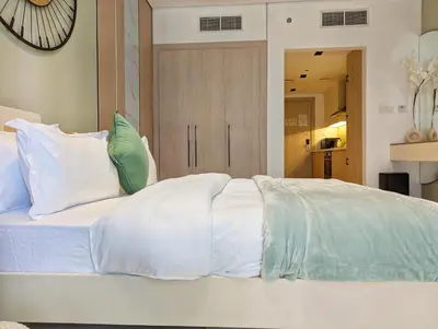 a white bed with pillows and a clock on the wall at Waterfront Studio with Burj Khalifa & Dubai Mall Access, Walk to Dubai Water Canal & Business Bay Metro in Dubai