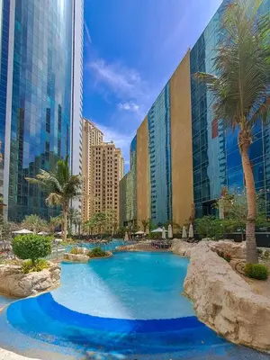 a swimming pool in front of a building with palm trees at JBR Coastal Escape - Amazing Sea Views, Pool & State-of-the-Art Gym in Dubai