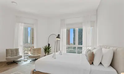 a white bedroom with a white bed and a couch at Spacious refurbished Studio steps away from metro in Dubai