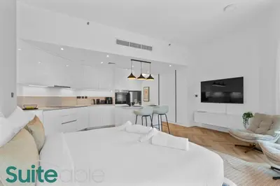 a white bedroom with a large bed and a kitchen at Spacious refurbished Studio steps away from metro in Dubai
