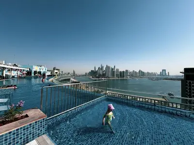 a child standing in a swimming pool next to a river at Seven Palm Apartment with Private Beach Access and Infinity Pool in Dubai