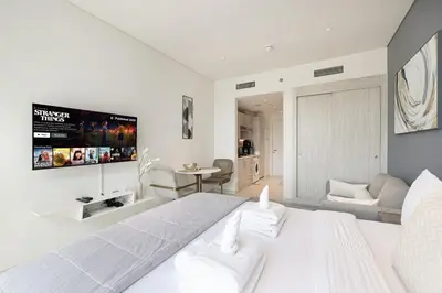 a white bedroom with a large bed and a flat screen tv at Seven Palm Apartment with Private Beach Access and Infinity Pool in Dubai