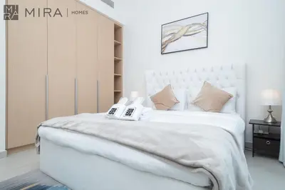 a white bedroom with a large white bed with a book at Mira Holiday Homes - Cosy 1BHK in the heart of Dubai Creek Harbour in Dubai