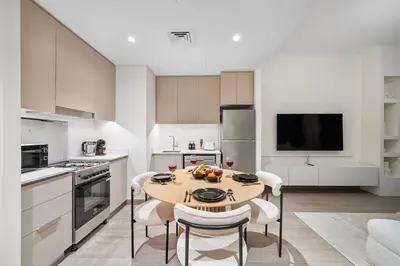 a white kitchen with a wooden table and chairs at FIRST CLASS 1BR Glamorous & Stylish Escape in Dubai