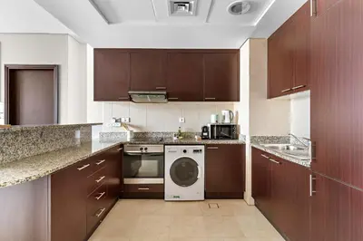 a kitchen with wooden cabinets and a washing machine at Silkhaus Premium 1BR at Sky Gardens in Heart of DIFC in Dubai
