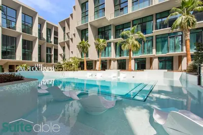 a swimming pool in front of a building with palm trees at Urban Retreat Studio in The Autograph JVC in Dubai
