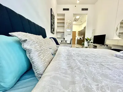 a bedroom with a white bed with blue pillows at Homes2Retreat - Stylish Studio Gym & Pool, JVC Dubai in Dubai