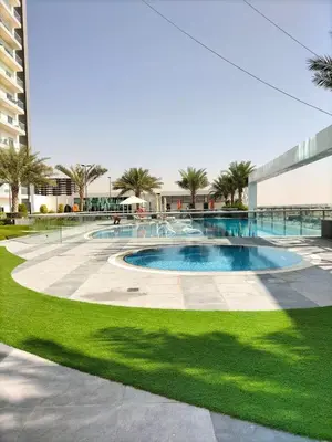 a swimming pool in the middle of a lawn with a building at Stylish Fully Furnished 1BH Apartment Close by Dubai Science Park, Dubai Miracle Garden and Butterfly Garden in Dubai