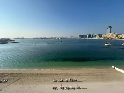 a group of people sitting on the beach near the water at Beach View 1BR at Beachfront 50 Off Eid Offer in Dubai