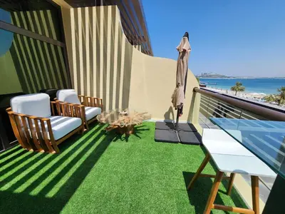 a balcony with chairs and an umbrella and grass at Bright Beachfront Studio with Breathtaking Views in Dubai
