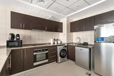 a kitchen with wooden cabinets and a stainless steel refrigerator at Silkhaus Dubai Marina 1BR in Bay Central West Tower in Dubai