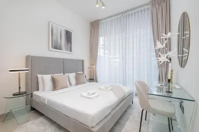 a white bedroom with a bed and a glass table at Stylish 1BHK by CzechIn Pool & Gym Prime JVC in Dubai