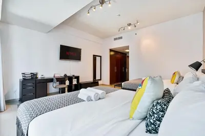 a bedroom with two white beds and a desk at Spacious 2 BR With Pool, Gym and Kid's Playground in Dubai