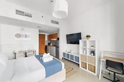 a white bedroom with a bed and a desk and a tv at Modern Studio in Production City in Dubai